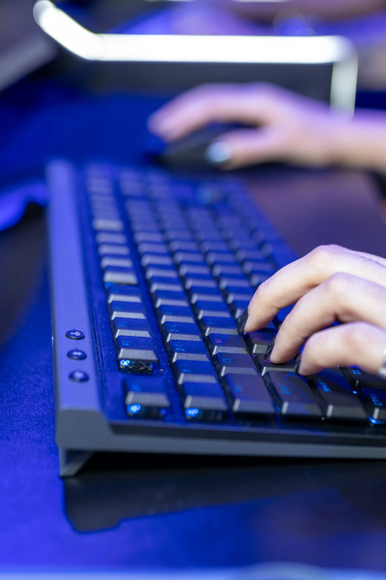 Close-up of hands typing on a backlit keyboard in blue light